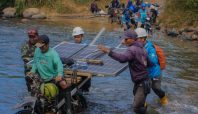 Petugas PLN dan warga bahu membahu membawa panel surya melintasi sungai. (Dok. PLN)
